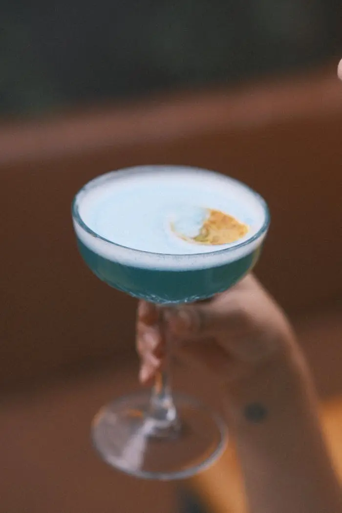 A person holding a blue cocktail in their hand